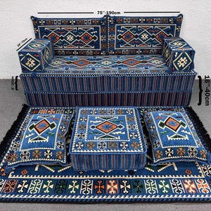 Op de afbeelding: Een blauw patroon bankstel met bijpassende kussens en een vloerkleed. De bank is 190 cm breed en 40 cm hoog. De set heeft geometrische ontwerpen in oranje, wit en groen.