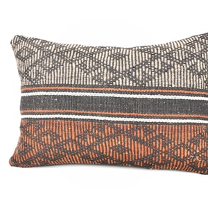 May include: Rectangular woven pillow with a geometric pattern in shades of brown, black, and white. The pillow features a diamond pattern at the top and bottom, with horizontal stripes in the middle.