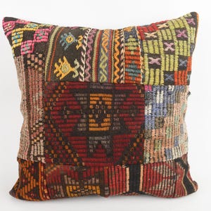 Puede incluir: Cojín decorativo cuadrado con diseño de patchwork. El cojín presenta una variedad de colores, incluyendo rojo, marrón, amarillo y azul. El diseño parece estar hecho de tela tejida, con patrones geométricos y florales.