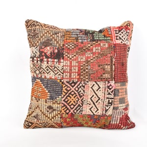 May include: Square decorative pillow with a patchwork design. The pillow features a variety of geometric patterns in shades of red, brown, orange, and beige. The pillow is made of a woven fabric and has a textured appearance.