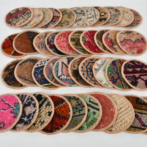 May include: A set of 30 round, colorful coasters made from recycled rug scraps. Each coaster features a unique pattern and is edged with a beige fabric trim.