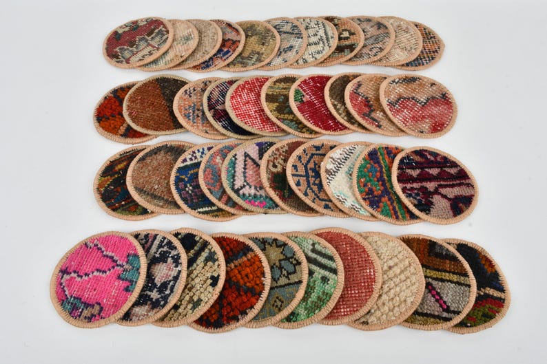 May include: A set of 30 round, colorful coasters made from recycled rug scraps. Each coaster features a unique pattern and is edged with a beige fabric trim.