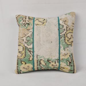 Puede incluir: Una almohada decorativa con un patrón floral verde, blanco y marrón. La almohada tiene un borde turquesa y está hecha de una tela suave y tejida.