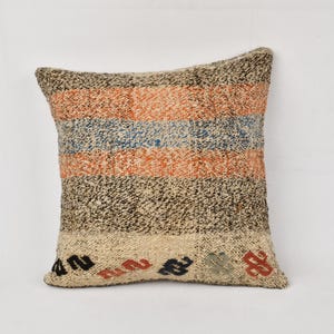 Op de afbeelding: Een decoratief kussen met een gestreept patroon in beige, oranje, blauw en zwart. Het kussen heeft een textuur en is versierd met kleine geborduurde details.