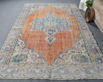 May include: A vintage rug with a faded orange background and a central medallion design in shades of blue, green, and white. The rug has a distressed look with a frayed border.