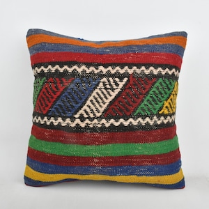 May include: A colorful throw pillow with a geometric pattern in shades of red, blue, green, yellow, and white. The pillow is made of woven fabric and has a fringed edge.
