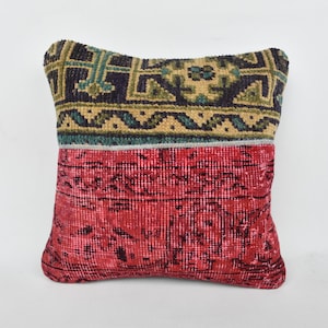 May include: A square pillow with a red and black floral pattern on one side and a green, blue, and yellow geometric pattern on the other side.
