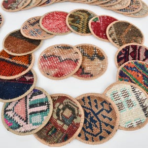 May include: A set of round, colorful coasters made from woven fabric with a beige border. The coasters are arranged in a circle pattern.