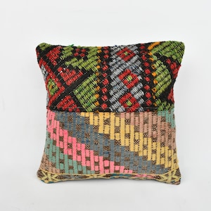Puede incluir: Una almohada de tiro colorida con un patrón geométrico en tonos de rojo, verde, azul, amarillo y rosa. La almohada está hecha de tejido tejido y tiene una forma cuadrada.