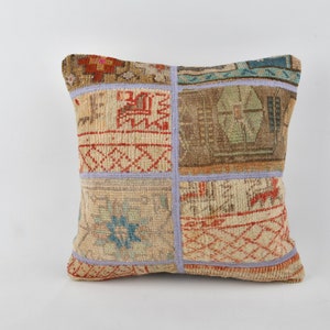 May include: A square throw pillow with a patchwork design. The pillow is made of a beige fabric with red, blue, and green accents. The pillow has a light purple border.