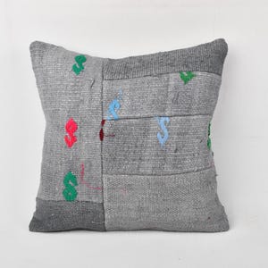May include: Gray decorative pillow with a patchwork design. The pillow features sections of varying shades of gray, with colorful embroidered accents in red, green, and blue. The pillow is square-shaped.