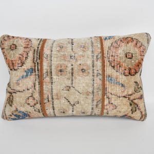 May include: Rectangular beige pillow with a floral pattern in orange, blue, and brown. The pillow has a woven texture and a vintage aesthetic, suitable for home decor.