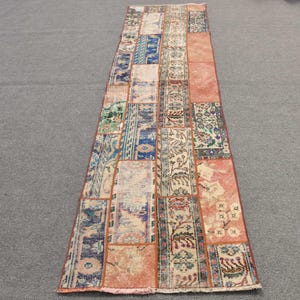May include: A long, rectangular rug with a patchwork design. The rug is made up of different colored squares and rectangles, with floral and geometric patterns. The rug is in shades of blue, red, orange, and white.