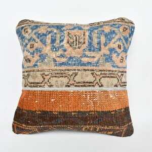 May include: A square throw pillow with a colorful geometric pattern. The pillow has a blue, orange, and brown design with a faded look.