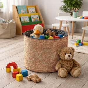 Op de afbeelding: Een ronde speelgoedbak met een patroon, gevuld met speelgoed, waaronder een pluchen eend, een houten paard en kleurrijke blokken. Een teddybeer zit naast de bak, met een houten auto en regenboogblokken op de vloer. Een houten boekenplank met boeken staat op de achtergrond.