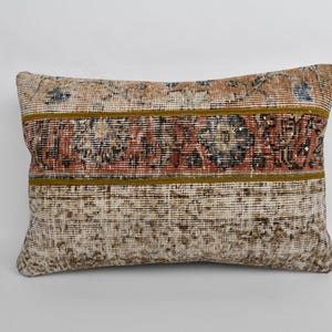 May include: Rectangular pillow with a vintage rug design. The pillow features a central band of red and black floral patterns, bordered by olive green stripes. The background is a mix of beige and faded colors.
