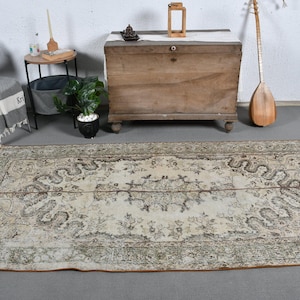 Puede incluir: Una alfombra vintage de color crema con un patrón floral marrón. La alfombra tiene un aspecto desgastado y está colocada sobre un suelo gris claro.