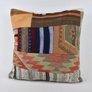 May include: A patchwork pillow cover with a variety of colors and patterns, including red, blue, green, and brown. The pillow cover is made of woven fabric and has a fringed edge.