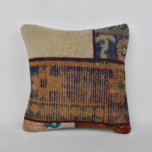 May include: A square throw pillow with a patchwork design. The pillow is made of a beige, brown, blue, and orange fabric with a woven texture.