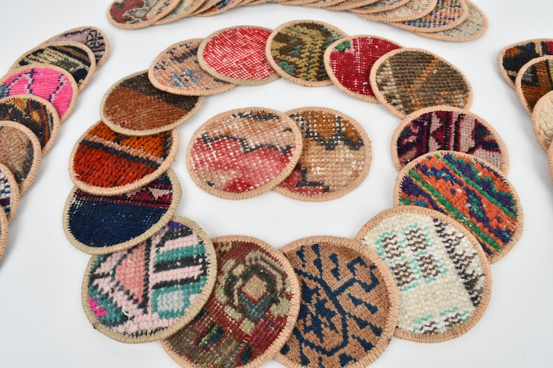 May include: A set of round, colorful coasters made from woven fabric with a beige border. The coasters feature various patterns and designs.