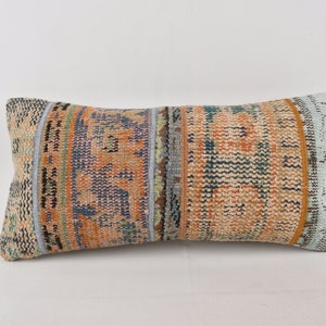 May include: A rectangular pillow with a colorful geometric pattern in shades of blue, orange, and green. The pillow is made from a woven fabric and has a light blue border.