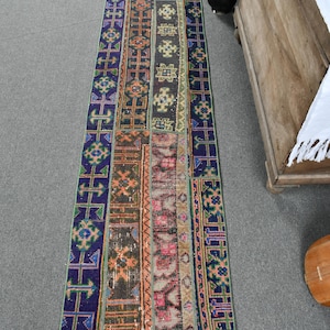 May include: A long, narrow rug with a patchwork design. The rug is made up of different strips of fabric, each with a unique pattern. The colors are mostly blue, green, orange, and red.