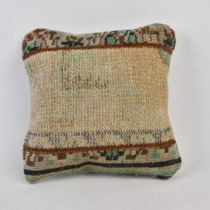 May include: A square throw pillow with a woven fabric cover. The pillow has a beige background with brown, blue, and green geometric patterns.