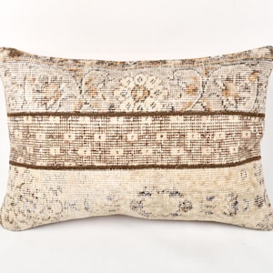May include: Rectangular cushion with a vintage-style design. The cushion features a cream, brown, and tan colour palette with a patterned design. The cushion has a distressed look, with a faded appearance.