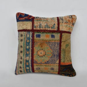 May include: A square throw pillow with a patchwork design. The pillow is made of different fabrics in shades of beige, brown, blue, and red. The fabric has a woven texture and features geometric patterns.