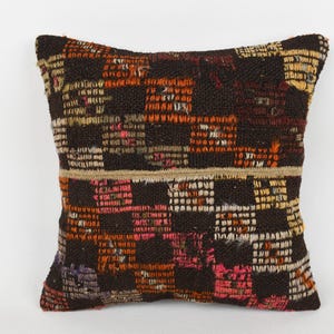 May include: Square decorative pillow with a woven, textured design. The pillow features a patchwork pattern in shades of brown, orange, pink, and beige. The pillow is a square shape and appears to be made of a durable fabric.