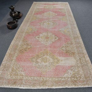 Puede incluir: Un corredor vintage de color rosa y crema con un patrón floral. La alfombra tiene un aspecto desgastado y está hecha de lana.