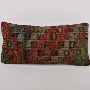 May include: A rectangular pillow with a colorful geometric pattern in shades of red, green, blue, and beige. The pillow is made of a woven fabric with a textured surface.