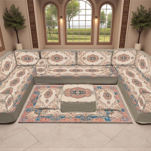 May include: U-shaped sofa with patterned cushions and a matching rug. The cushions have a cream background with a floral design in peach, blue, and brown. The sofa and rug are in a room with arched windows and a view of trees.