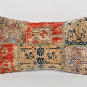 May include: Rectangular decorative pillow with a patchwork design. The pillow features a mix of colors including red, beige, and blue. The design includes geometric and floral patterns, creating a vintage or bohemian aesthetic.