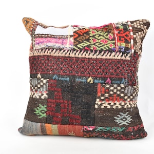 May include: A square patchwork cushion with a variety of colours and patterns. The cushion features a mix of textures and designs, including geometric shapes, stripes, and floral motifs. The colour palette includes red, brown, black, and touches of green and pink.
