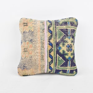 Puede incluir: Una pequeña almohada cuadrada con fondo beige y un patrón geométrico colorido en tonos azules, verdes y rosas.