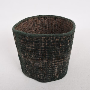 May include: A woven basket with a dark green exterior and a brown interior. The basket has a slightly irregular shape and a textured surface. The rim is reinforced with a darker green trim. The basket is suitable for storage.