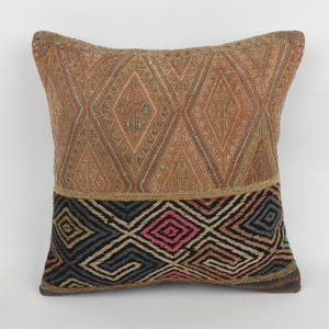 May include: Square decorative pillow with a geometric pattern. The top half features a diamond pattern in shades of brown, while the bottom half has a black, blue, and pink geometric design. The pillow is a home decor item.