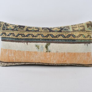 May include: A rectangular pillow with a colorful geometric pattern in shades of brown, blue, green, and beige. The pillow has a white and orange stripe in the center.
