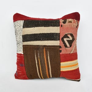 May include: A patchwork pillow cover with a red, brown, white, and black geometric pattern. The pillow cover is made of woven fabric and has a fringed edge.