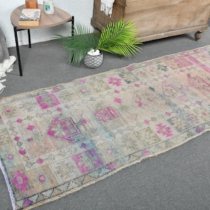 May include: A vintage Turkish runner rug with a faded pink, blue, and cream color scheme. The rug has a traditional geometric pattern and is perfect for adding a touch of bohemian style to any room.