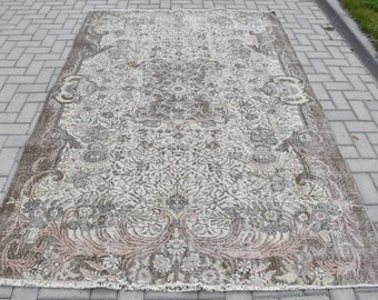 May include: A vintage rug with a floral pattern in shades of brown, beige, and pink. The rug has a fringed edge and is laid out on a gray brick surface.