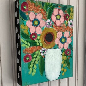 May include: A rectangular wooden wall art piece featuring a painted floral arrangement in a white vase against a teal background. The flowers are rendered in shades of pink, orange, and yellow with green foliage. The side edge is black with white dots.