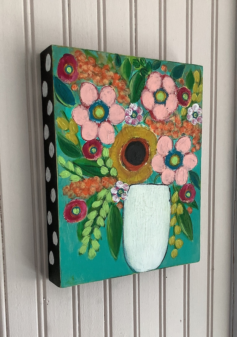 May include: A rectangular wooden wall art piece featuring a painted floral arrangement in a white vase against a teal background. The flowers are rendered in shades of pink, orange, and yellow with green foliage. The side edge is black with white dots.