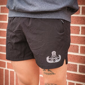 May include: Black athletic shorts with a white embroidered EOD badge on the right leg. The shorts have a zippered pocket on the right side.
