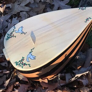 May include: A wooden stringed instrument with a pear-shaped body and black and brown stripes. The instrument is decorated with two white doves and green leaves with red berries.