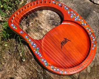 May include: A wooden lyre with a red finish and a floral design. The lyre has a round soundboard and a curved neck with tuning pegs. The lyre is decorated with blue and gold flowers.
