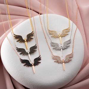 May include: A collection of angel wing necklaces in various metallic finishes. The necklaces feature detailed wing pendants with either black, clear, or rose-colored stones. The chains are gold, silver, and rose gold.