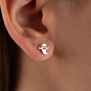 May include: Gold ghost stud earrings. The ghost has a white outline and a black face with two eyes and a mouth.