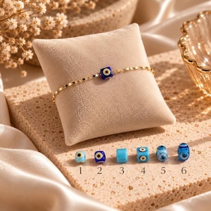 May include: A gold-toned chain bracelet featuring a single square blue and white evil eye bead. Below, six individual beads are displayed in a row, numbered one through six, showcasing various blue and white evil eye designs.